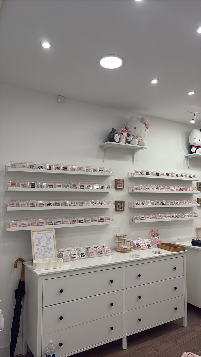 Le mur de la boutique : huit longues étagères de boîtiers, peluches Hello Kitty et commode blanche.